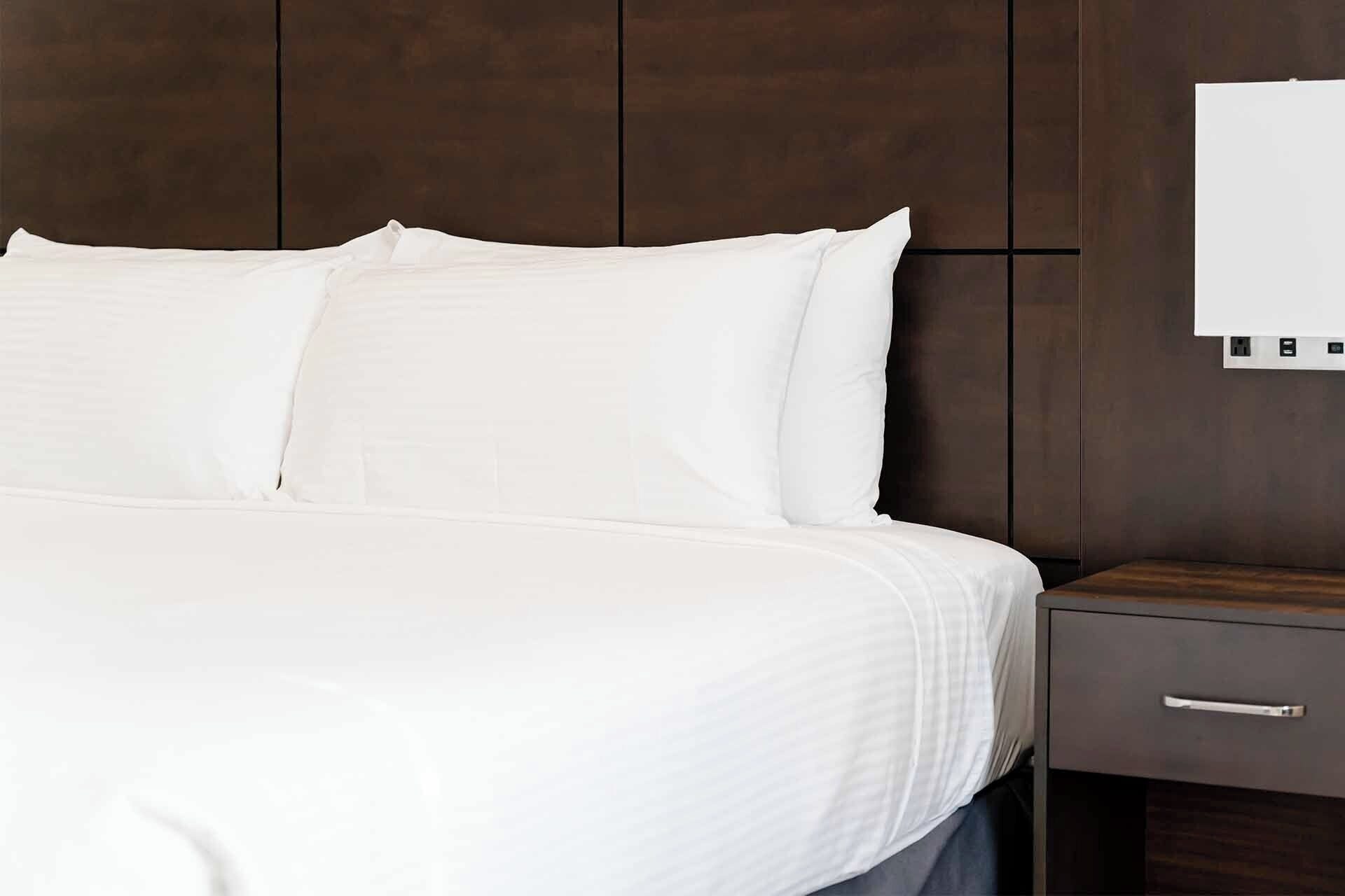 A neatly made bed with white linens, a wooden headboard, and a nightstand with a drawer.