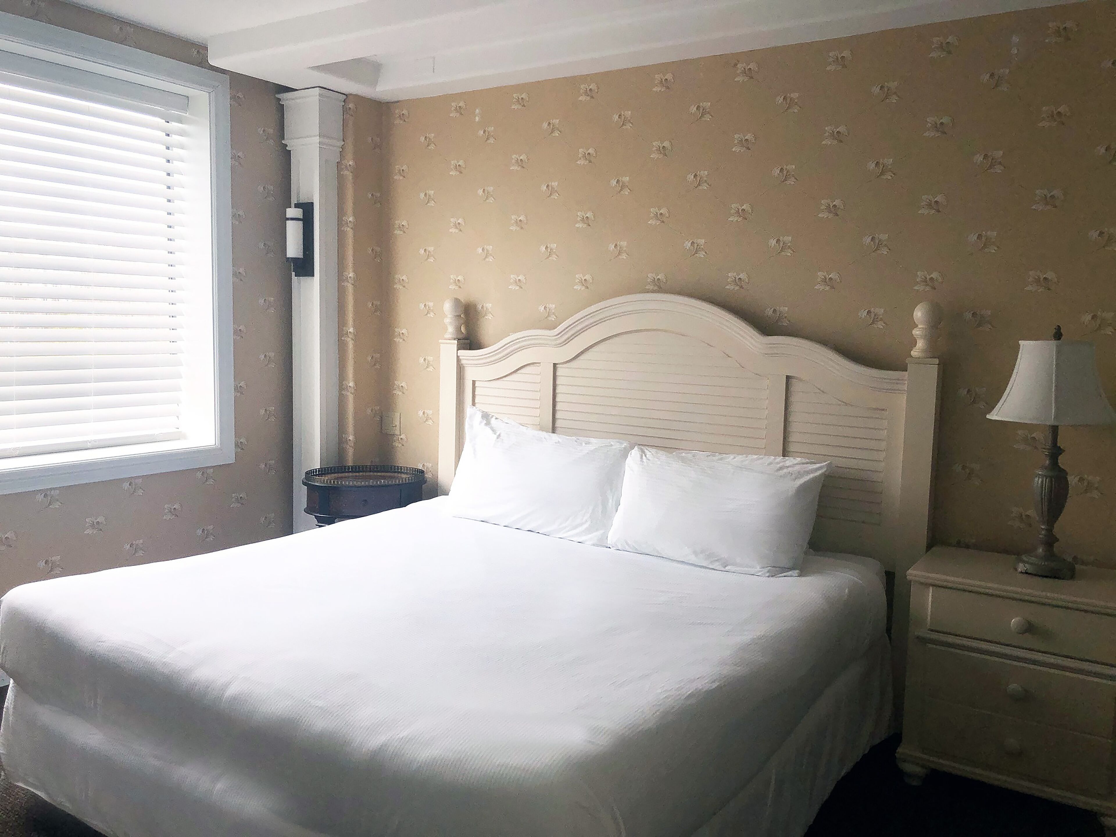 A neatly made bed with white linens, a wooden headboard, and a nightstand with a lamp.