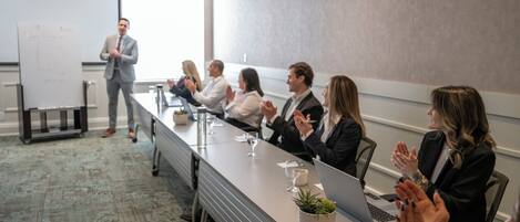 A conference room with a long table, a projector screen, and attendees clapping.