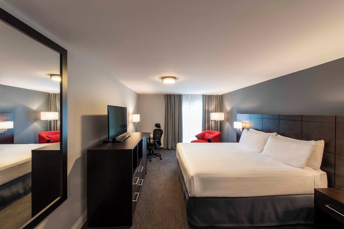 Een hotelkamer met een groot bed, een bureau met stoel, een televisie en een spiegel.