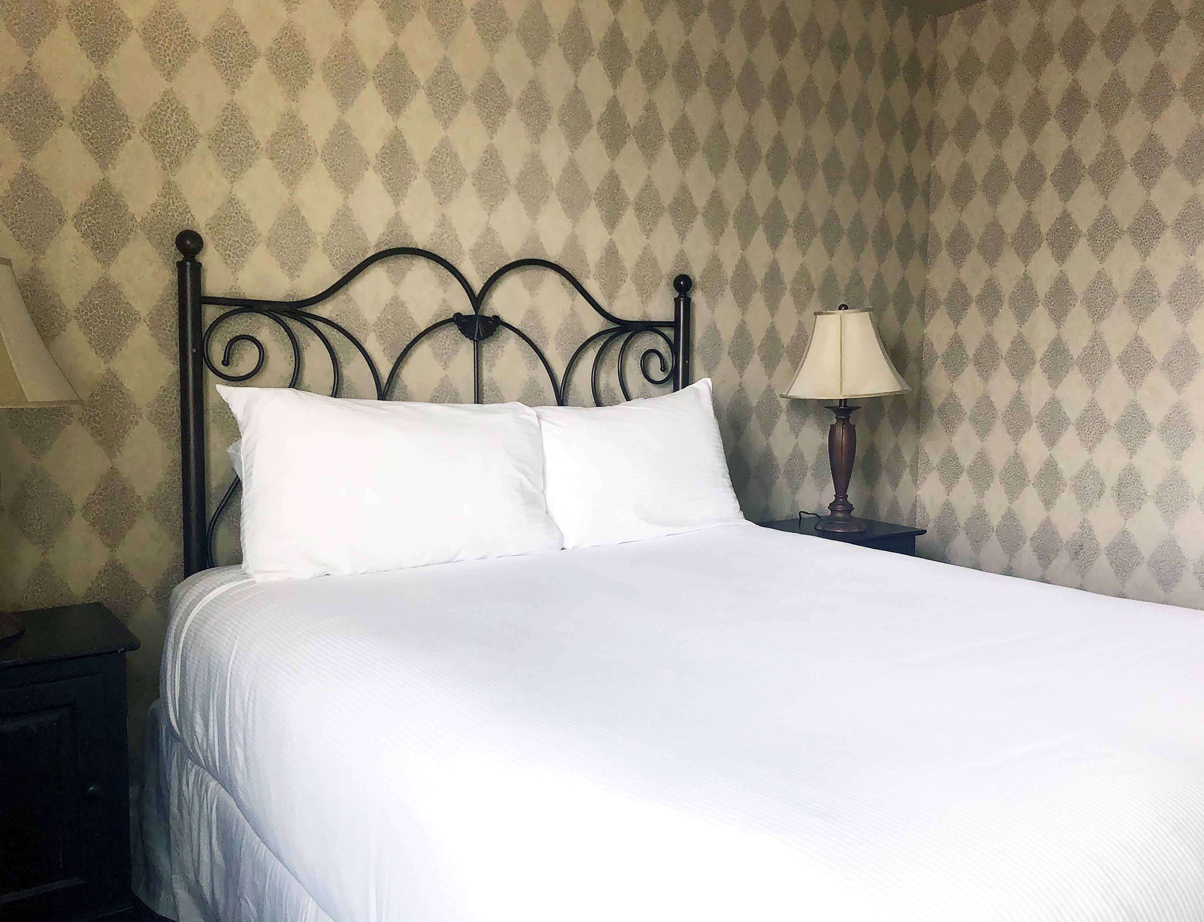 A neatly made bed with white linens, a metal headboard, and a bedside lamp on a nightstand.