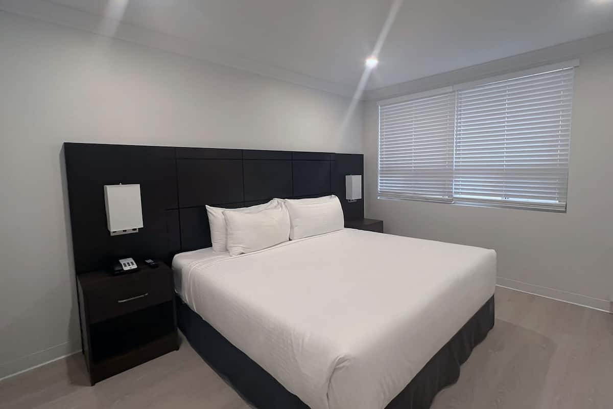 Een slaapkamer met een bed, nachtkastjes, een wandlamp en een raam met jaloezieën.
