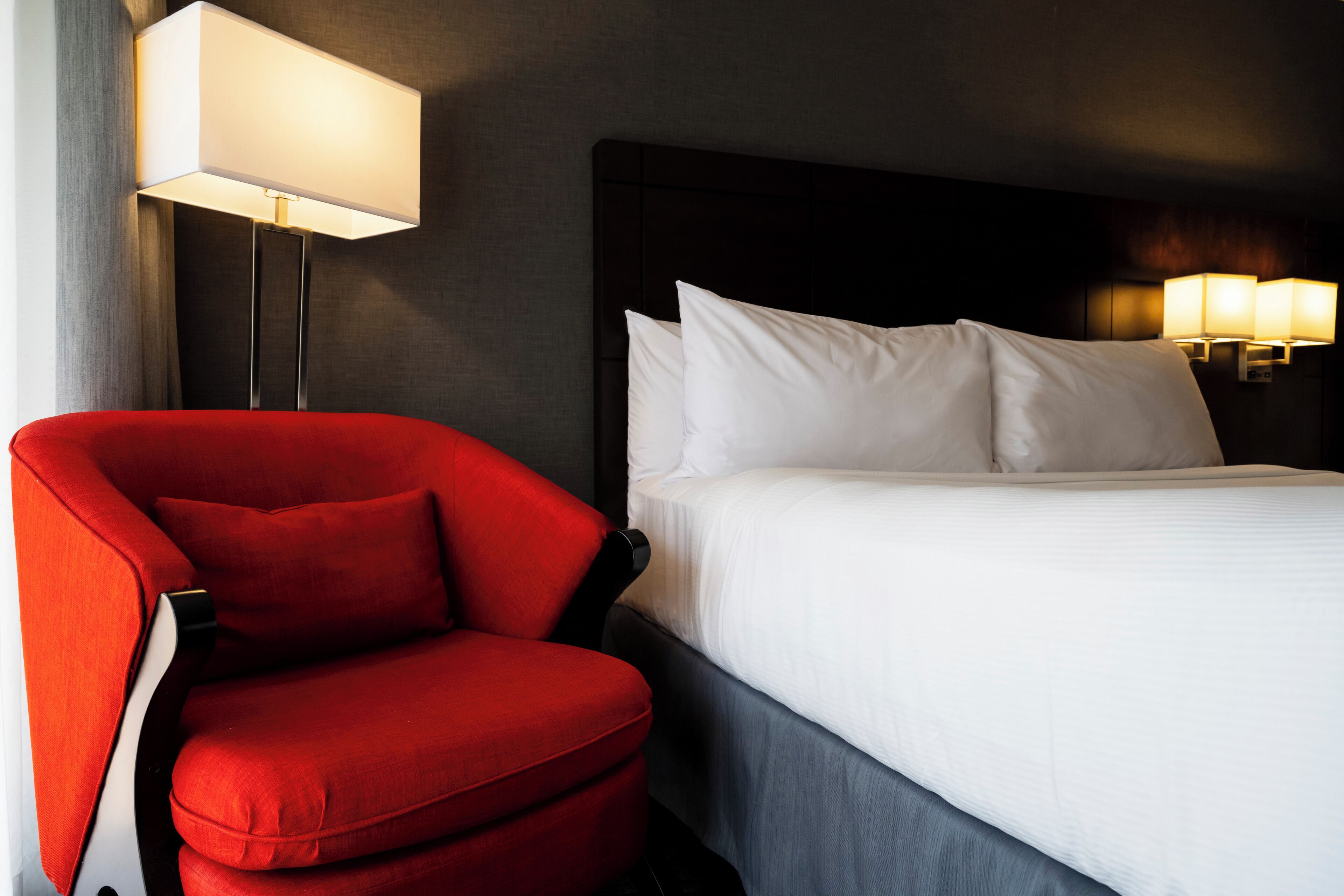 A hotel room with a large bed, a red armchair, and two wall-mounted lamps.