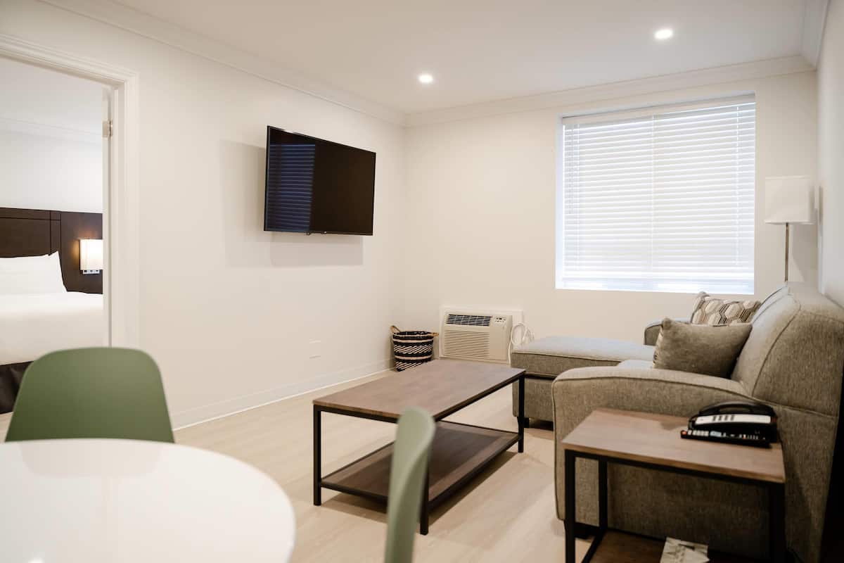 Een moderne hotelkamer met een bed, een flatscreen televisie aan de muur, een bank, een kleine tafel en een raam met zonwering.