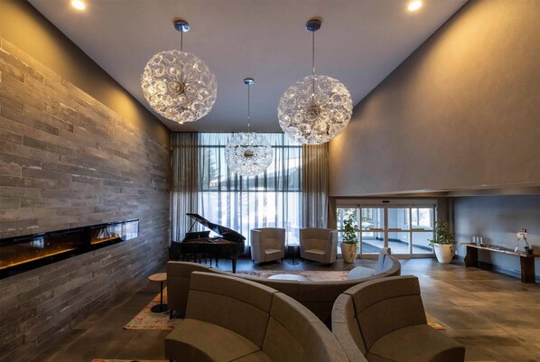 A modern living room with a grand piano, a fireplace, and a large chandelier.