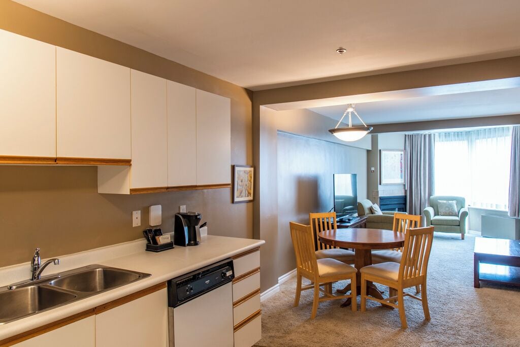 Una cocina moderna con lavavajillas, cafetera y un comedor con una mesa redonda y sillas.