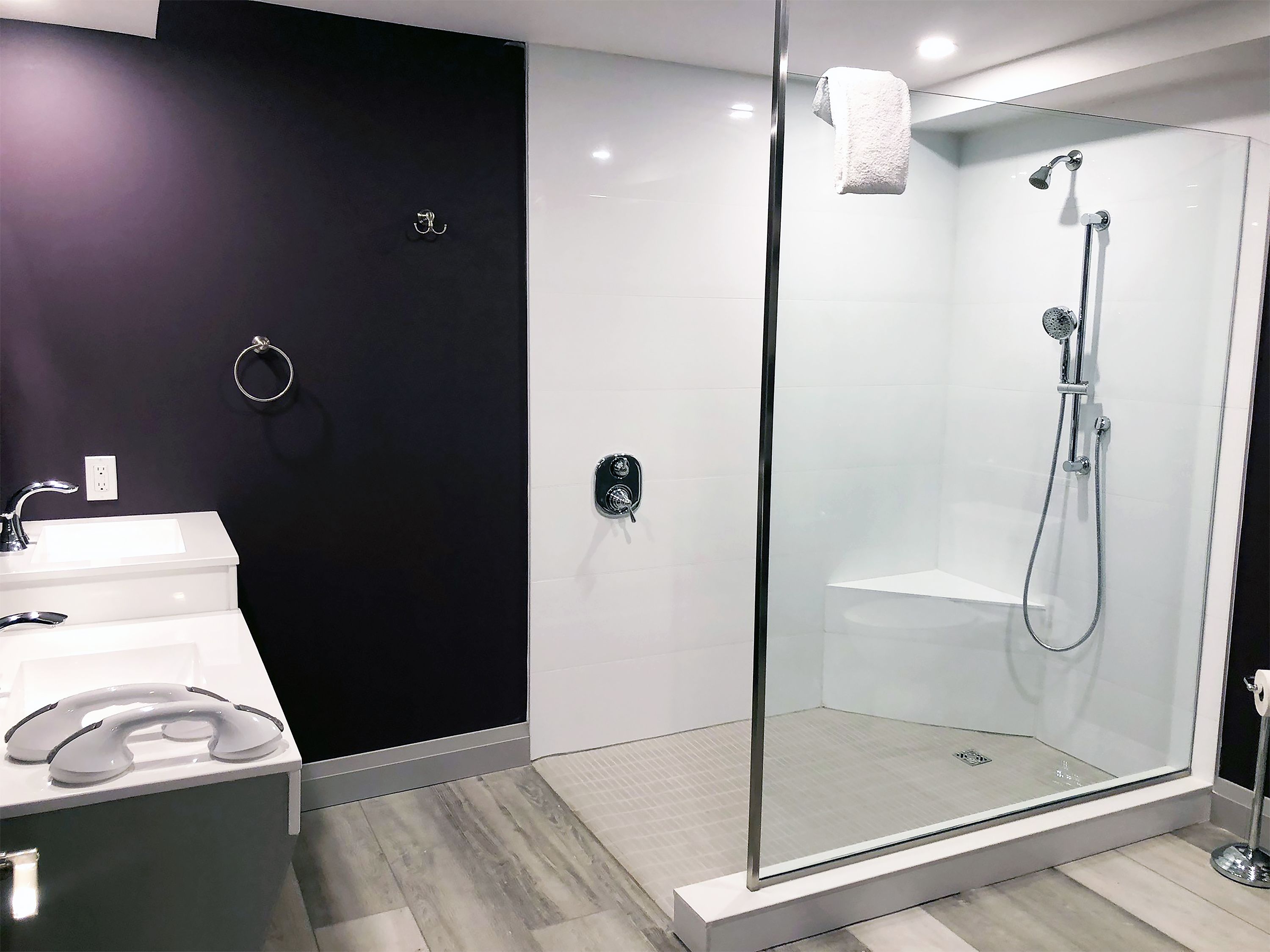 Un bany modern amb dutxa tancada amb vidre, un lavabo blanc i una paret d'accent fosc.