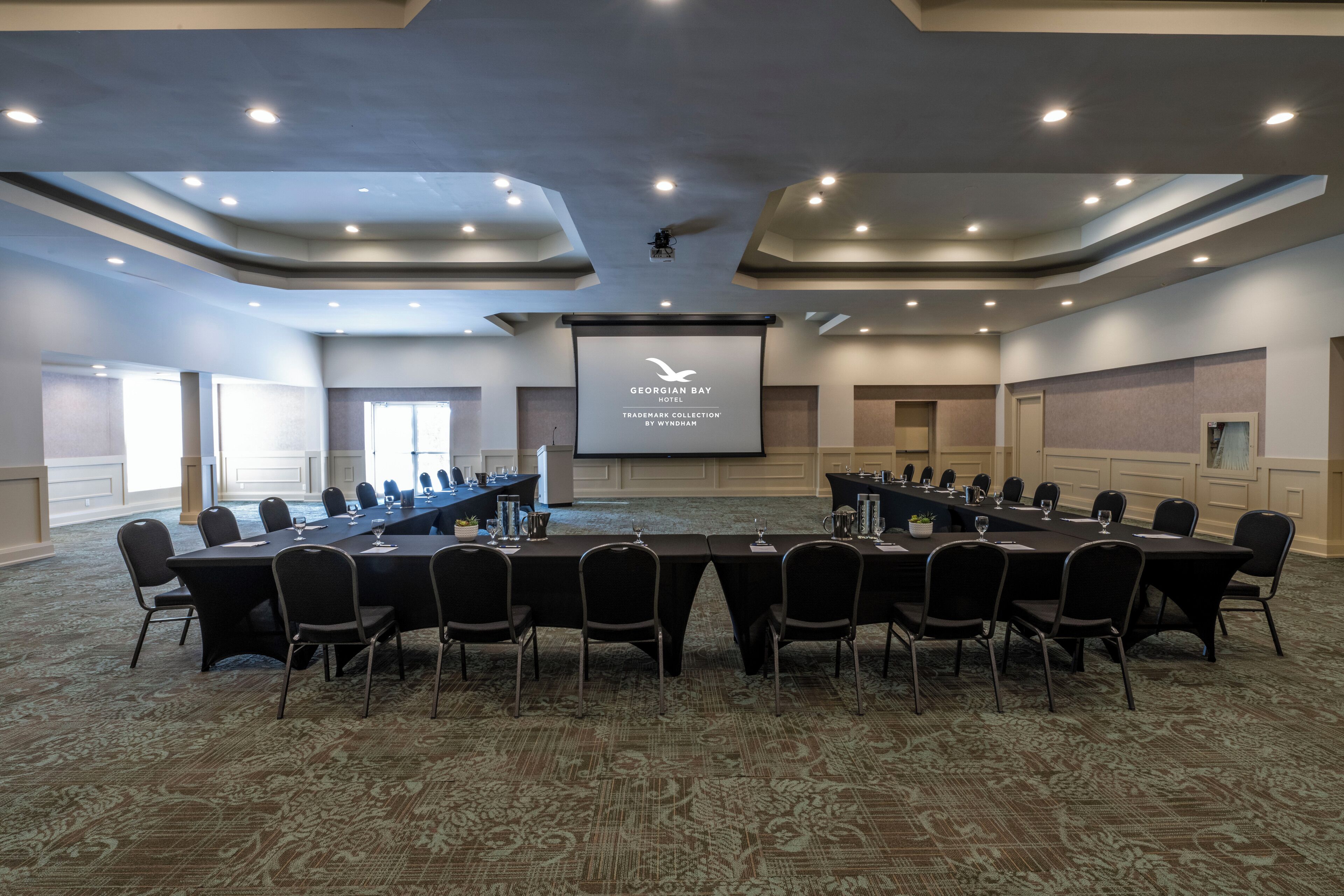 Une salle de conférence d’un hôtel situé dans la région de la baie géorgienne, équipée d’une longue table, de chaises et d’un écran de projection.