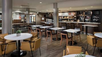 A modern restaurant with round tables and chairs, a bar area, and a kitchen in the background.