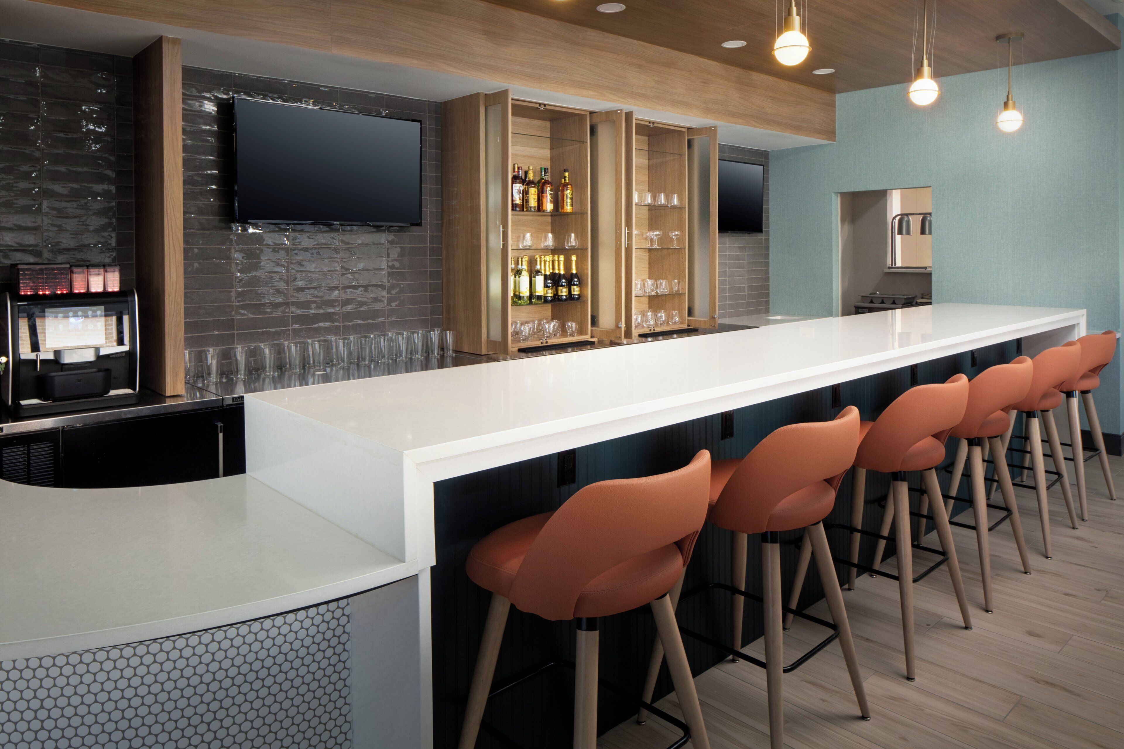 A modern bar area with a long counter, bar stools, a television mounted on the wall, and a wine and glass display cabinet.