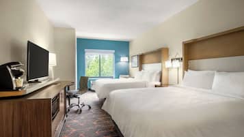 A hotel room with two beds, a desk with a TV, a chair, and a window with a view of greenery.