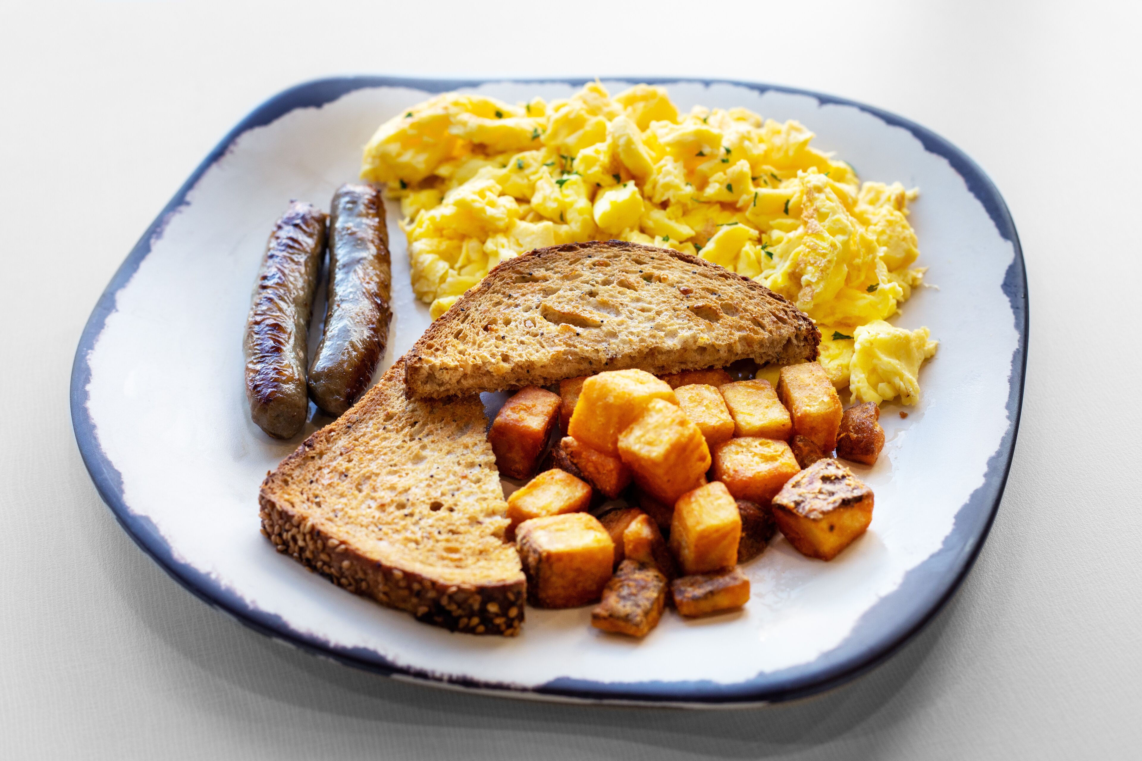 Ein Teller mit Rührei, Würstchen, Toast und Bratkartoffeln.