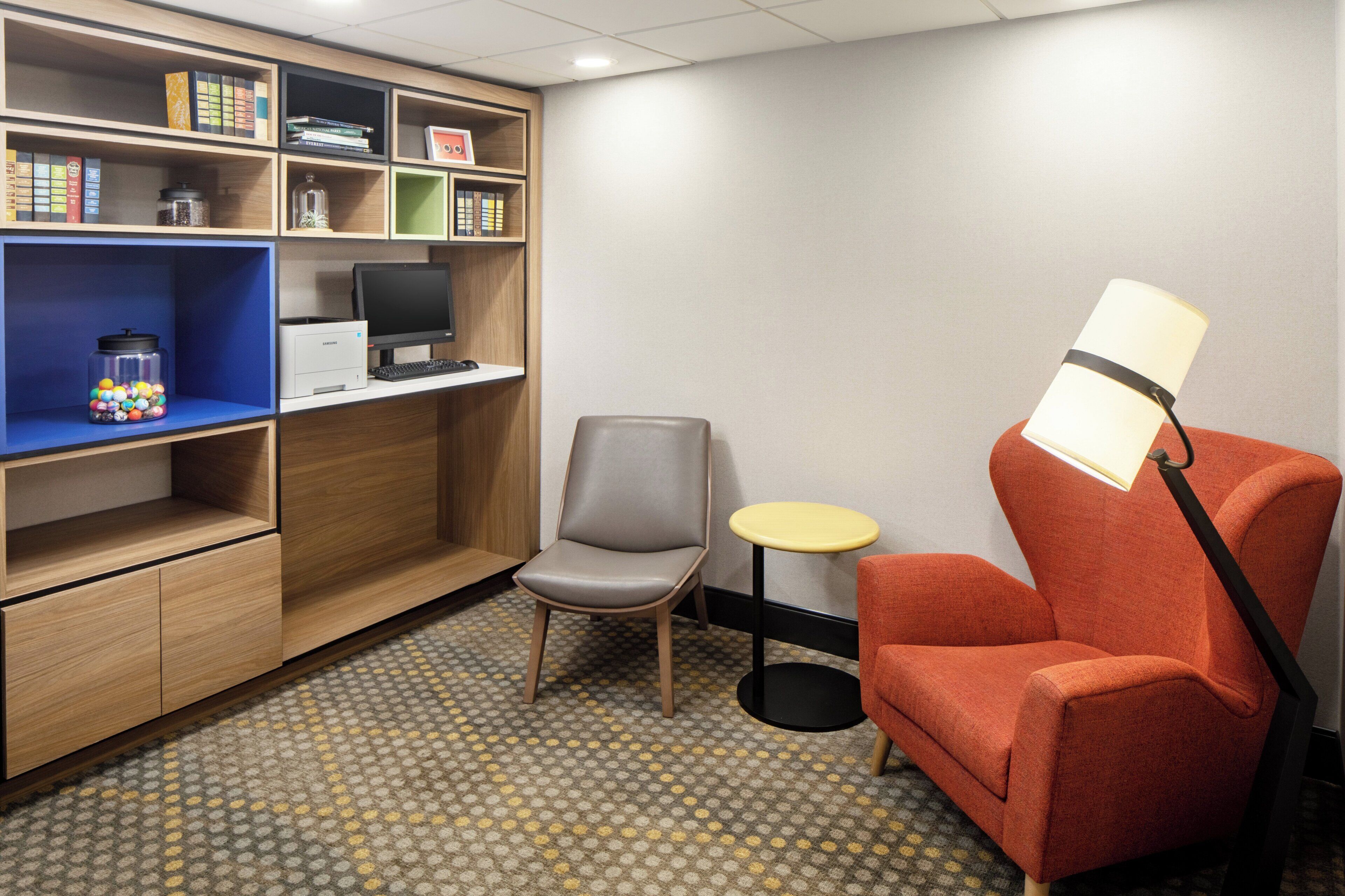A small room with a desk, chair, lamp, and shelves with books and a jar of marbles.