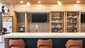 A modern bar area with a white countertop, three brown bar stools, a mounted TV, and a liquor display cabinet. - Holiday Inn Cheshire - Southington by IHG (Southington)