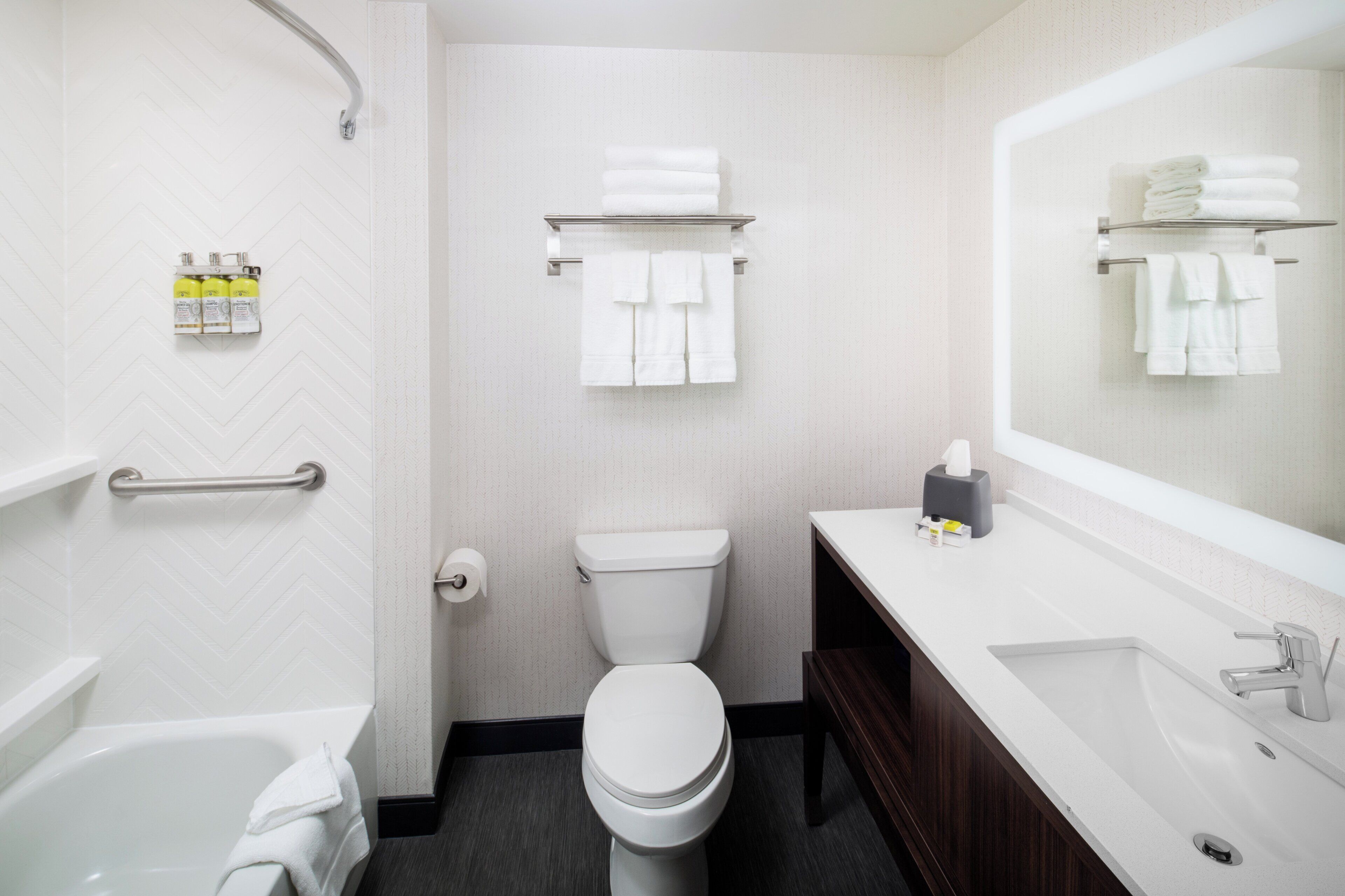 A modern bathroom with a white toilet, a bathtub, a vanity with a mirror, and a towel rack.
