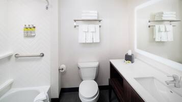 A modern bathroom with a white toilet, a bathtub, a vanity with a mirror, and a towel rack.