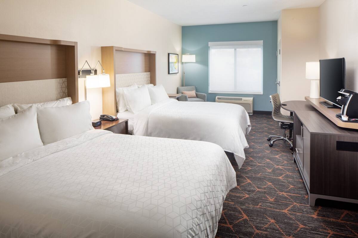 A hotel room with two beds, a desk with a computer, a chair, a TV, and a window with blinds.