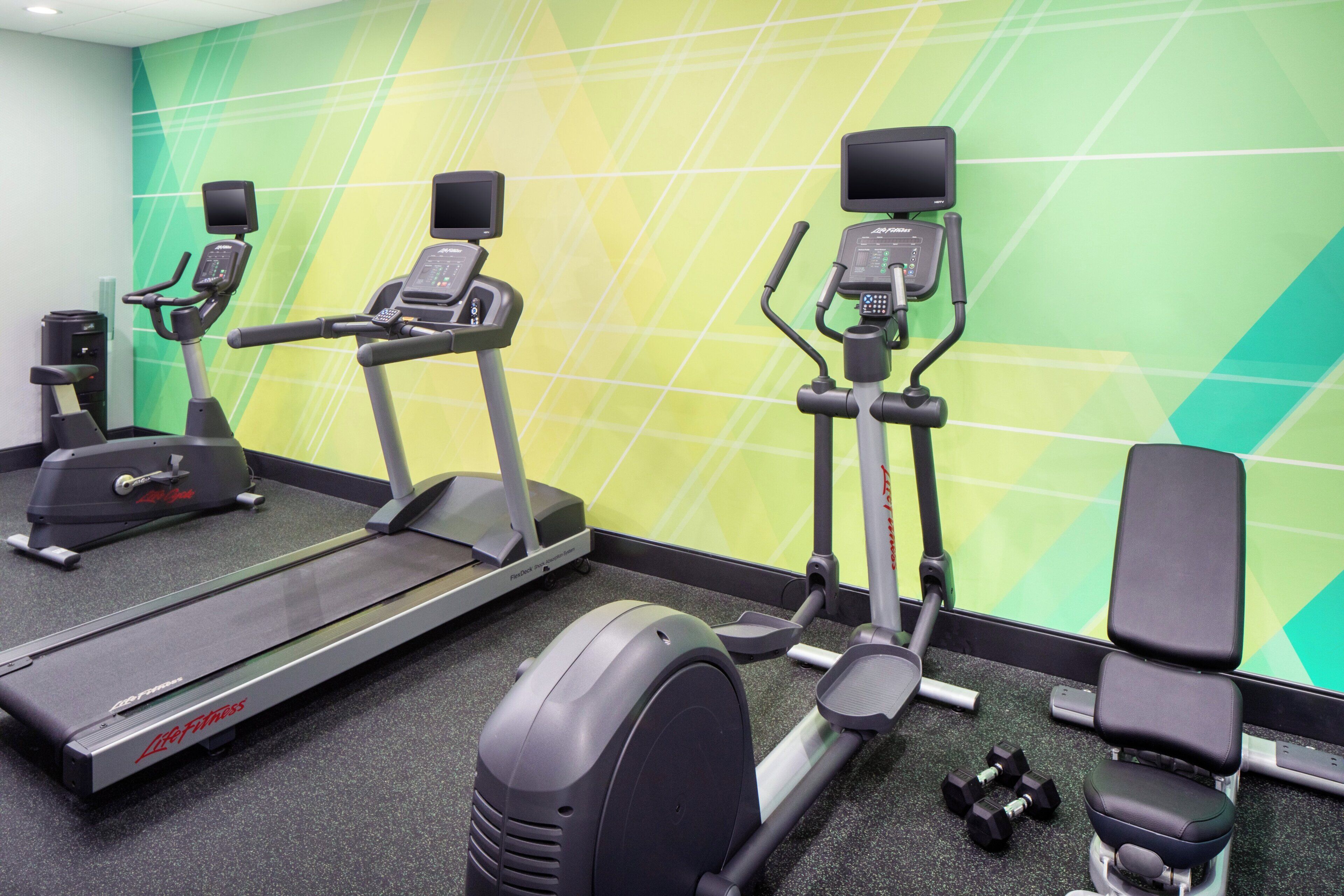 Un gimnasio con cintas de correr, elíptica, banco y mancuernas.