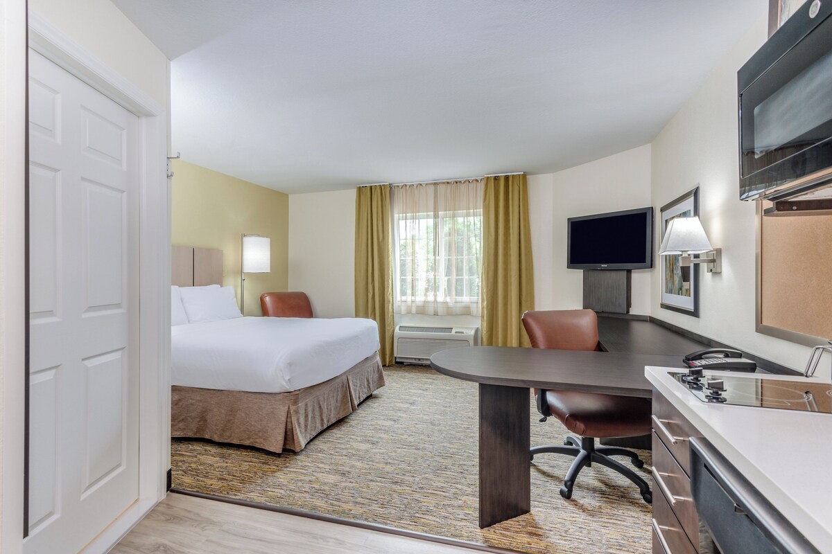 Habitación de hotel con cama, escritorio, silla, televisor y aire acondicionado.