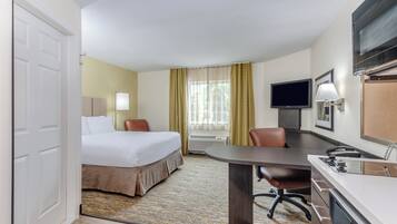 A hotel room with a bed, desk, chair, television, and air conditioning unit.