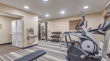A hotel gym with exercise equipment, a bench, and a water dispenser.