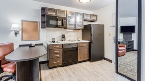 A compact kitchen with a microwave, refrigerator, and built-in oven. There is a small dining area with a table and chairs. - Candlewood Suites Secaucus - Meadowlands by IHG (Secaucus)