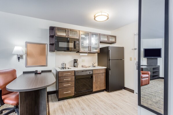 Una cocina compacta con microondas, refrigerador y horno empotrado. Hay un pequeño comedor con mesa y sillas.
