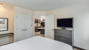 Habitación de hotel con cama, televisor, cómoda y puerta que da a una kitchenette.