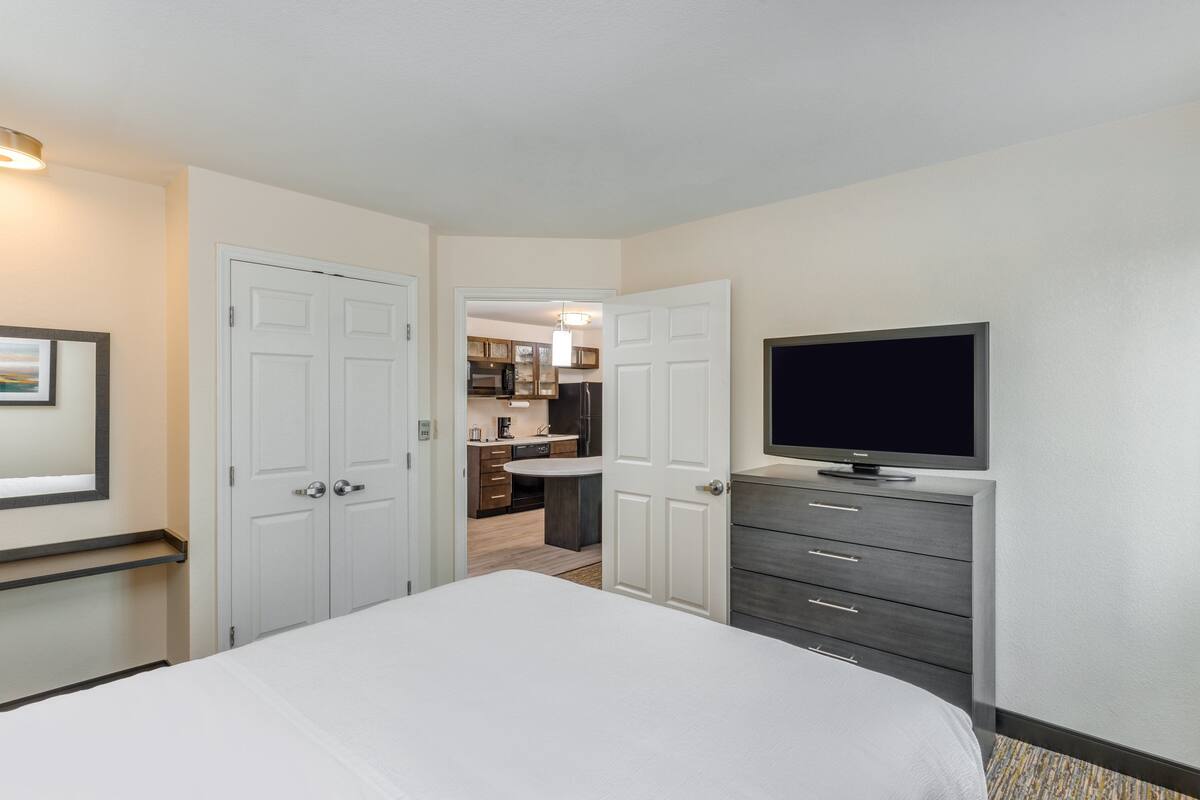 Habitación de hotel con cama, televisor, cómoda y puerta que da a una kitchenette.
