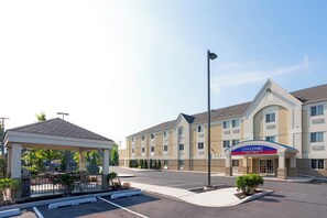 Ein Hotel Eingangsbereich mit überdachtem Wartebereich, einem Parkplatz und einem Gebäude, das Candlewood Suites ausweist.