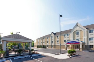 Entrada de hotel con área de espera techada, estacionamiento y un edificio con el letrero de Candlewood Suites.