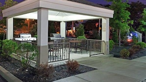 Un patio exterior cubierto con una parrilla, una zona de estar y vistas del paisaje circundante.