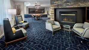 En modern hotellobby med en eldstad i sten, bekväma sittplatser, en matplats och en stor TV-skärm.