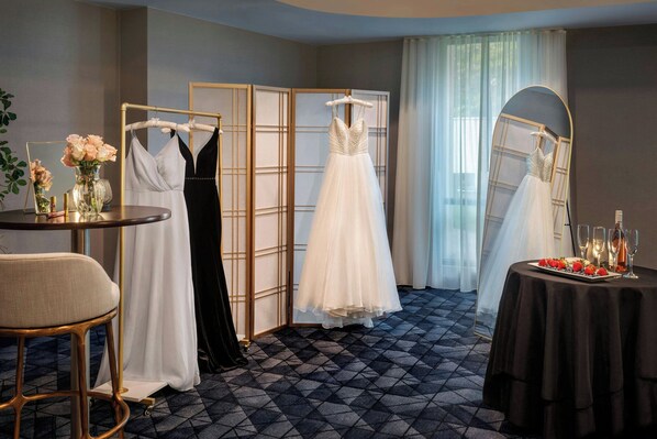 A room with a round table, a chair, and three dresses on hangers.