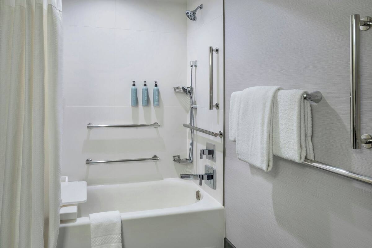 A modern bathroom with a bathtub, a shower, and handrails.