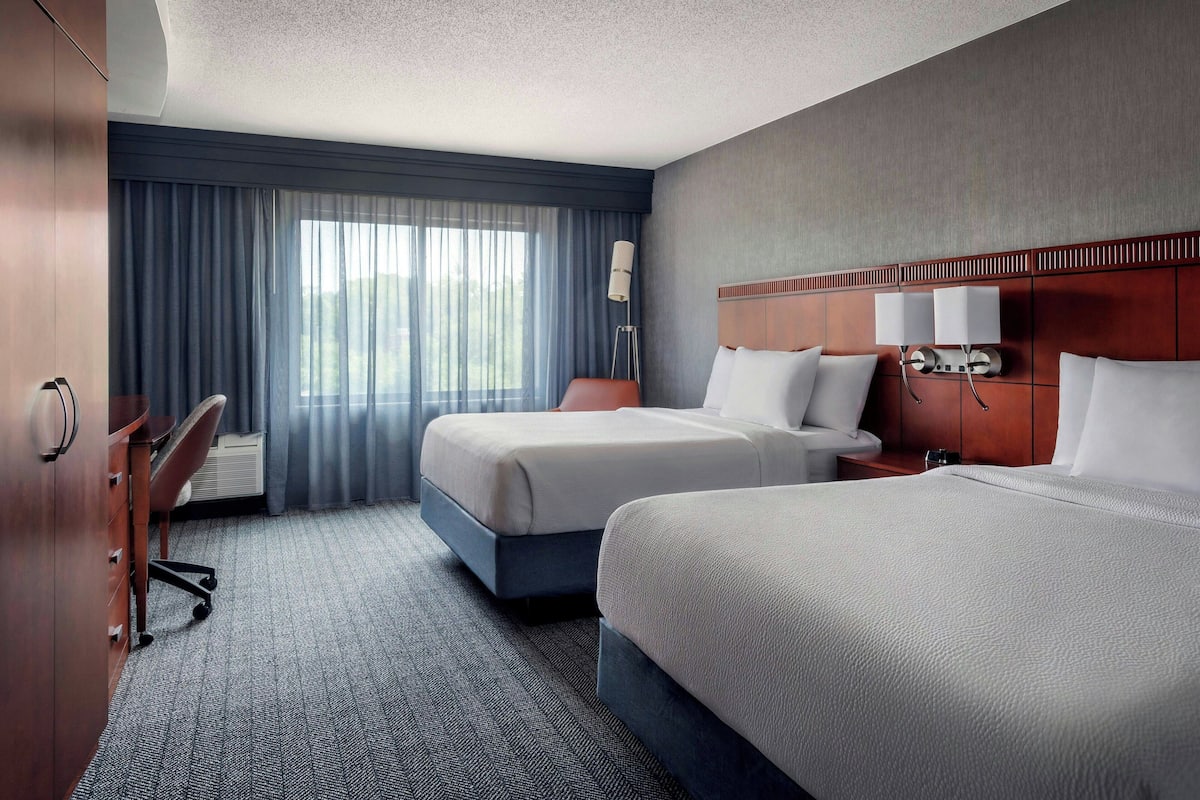 A hotel room with two beds, a desk, and a chair.