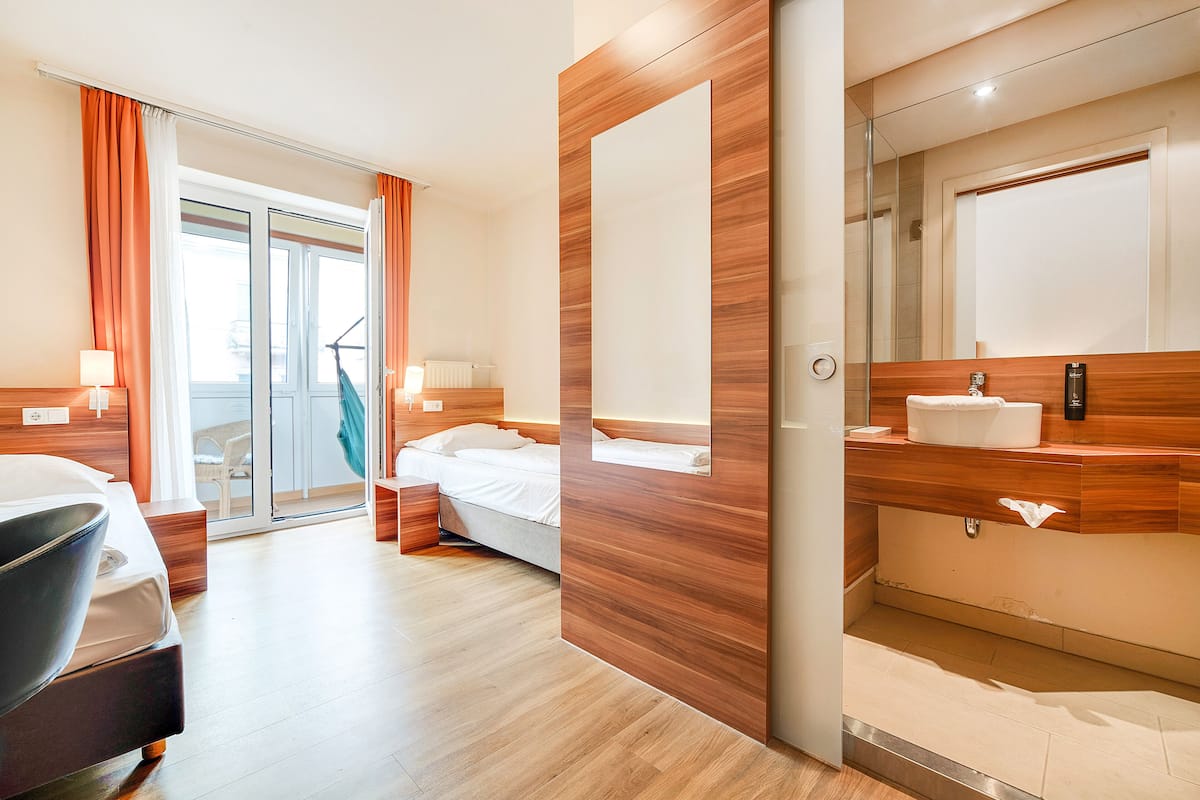 Hotelkamer met een bed, een bureau, een stoel, een badkamer met spiegel en een glazen schuifdeur die leidt naar een balkon.