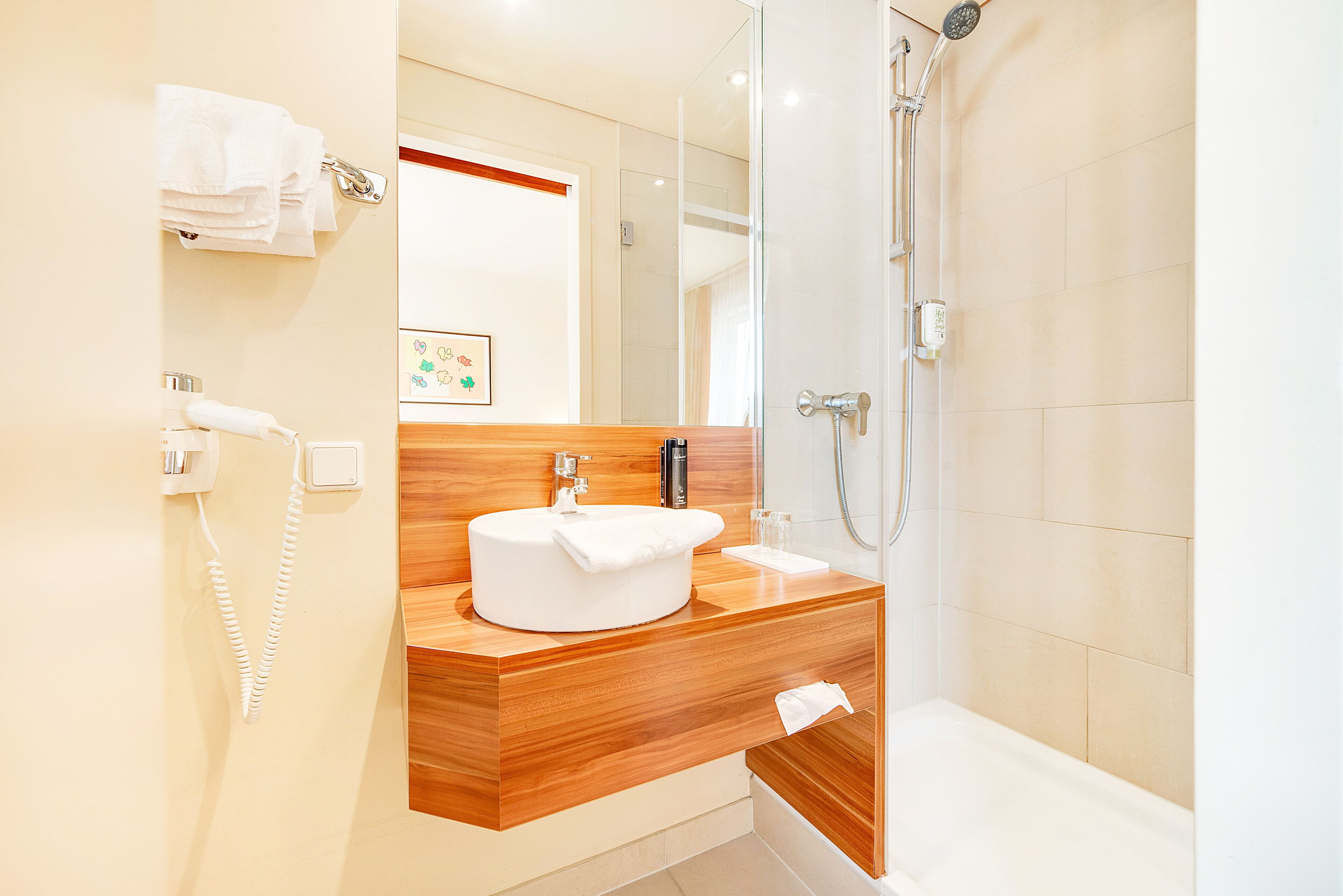 Un baño moderno con tocador de madera, lavamanos blanco y cabina de ducha con puertas de vidrio.