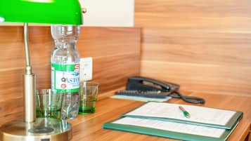 Un mostrador de recepción de madera con una lámpara de escritorio verde, una botella de agua, dos vasos, un teléfono y una libreta con un bolígrafo.