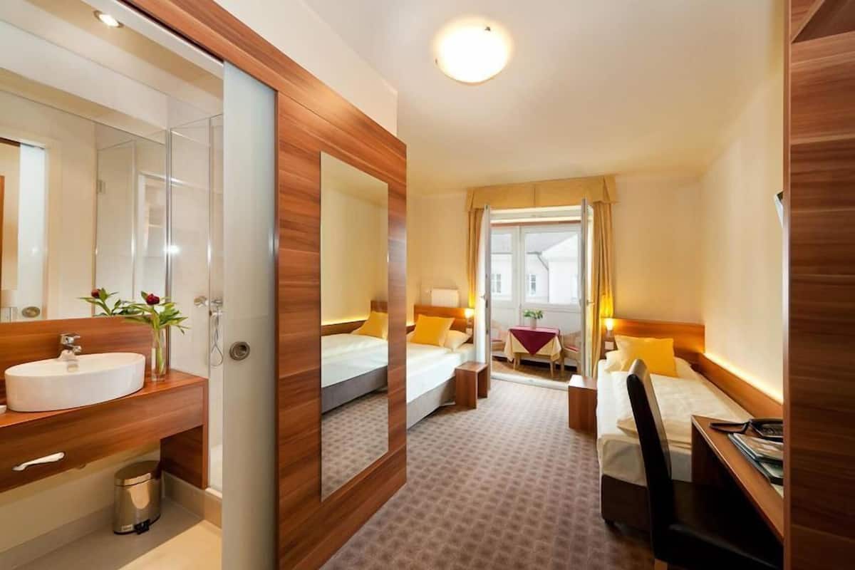 Habitación de hotel con tocador de madera, un espejo grande, una cama con almohada roja y amarilla, una mesita con una planta y un escritorio con silla.