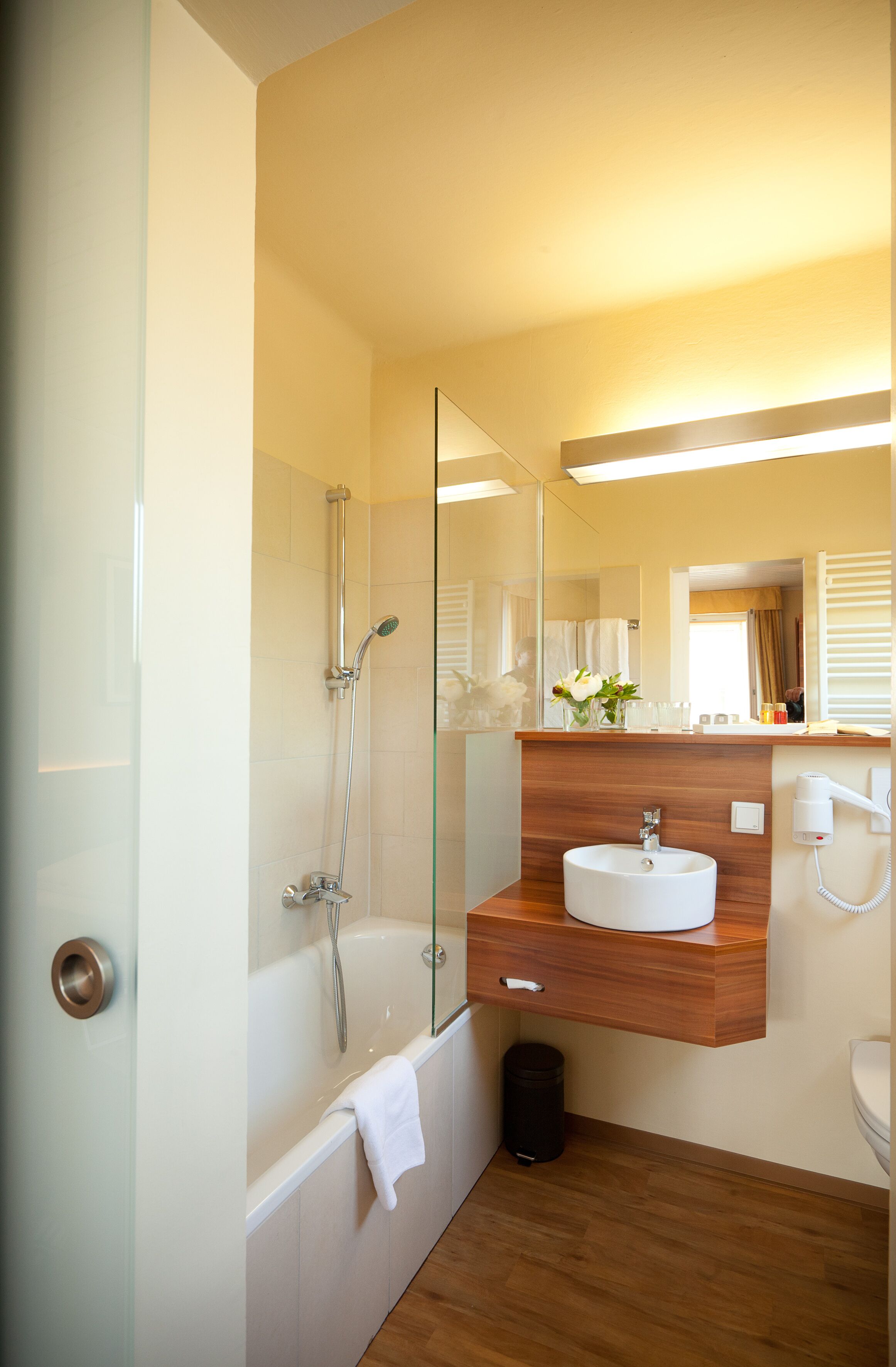 A modern bathroom with a glass-enclosed shower, a white sink, and a wooden vanity.