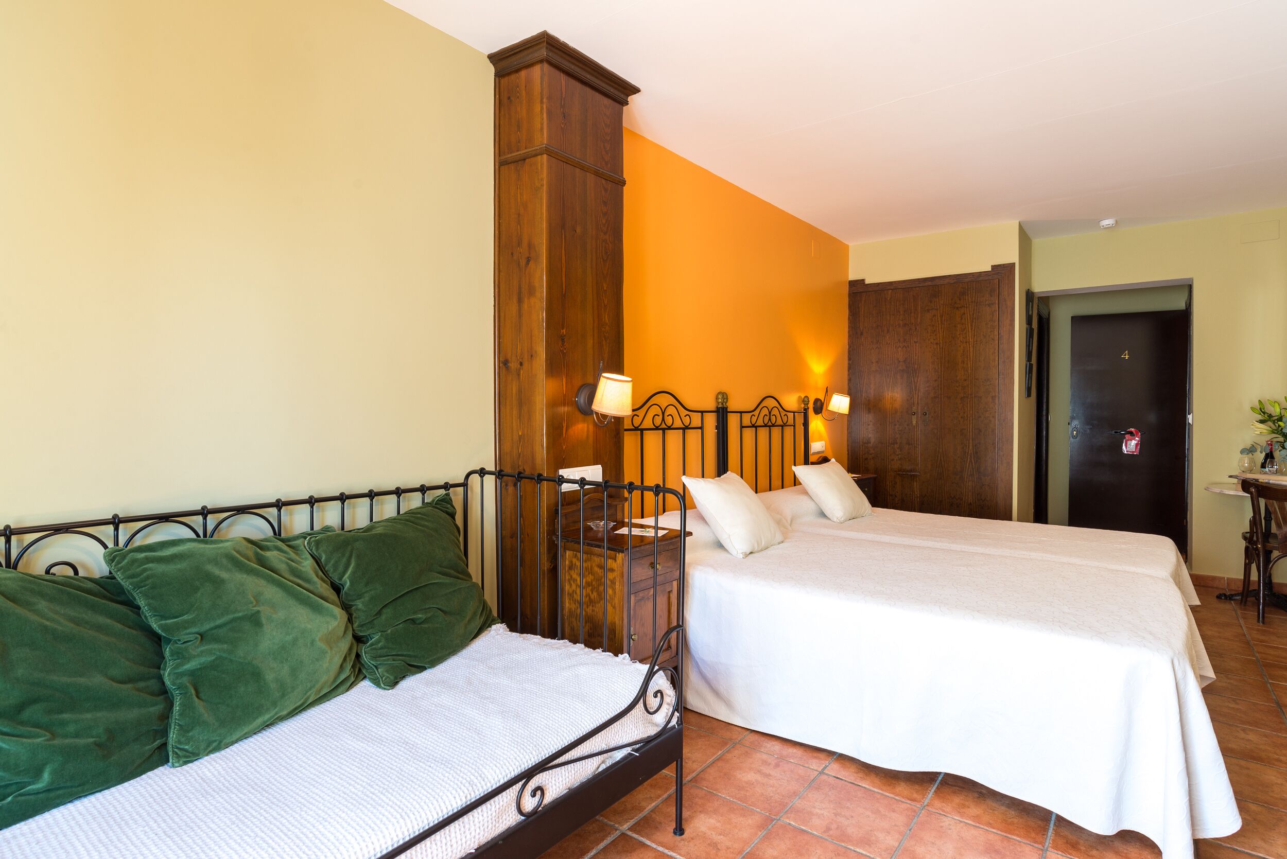 A hotel room with two beds, a wooden wardrobe, and a small table with a lamp.