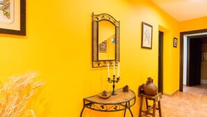 A hallway with a bright yellow wall, a round table with a mirror and candles, and a chair. - Hostel El Escudo de Mijas (Mijas)