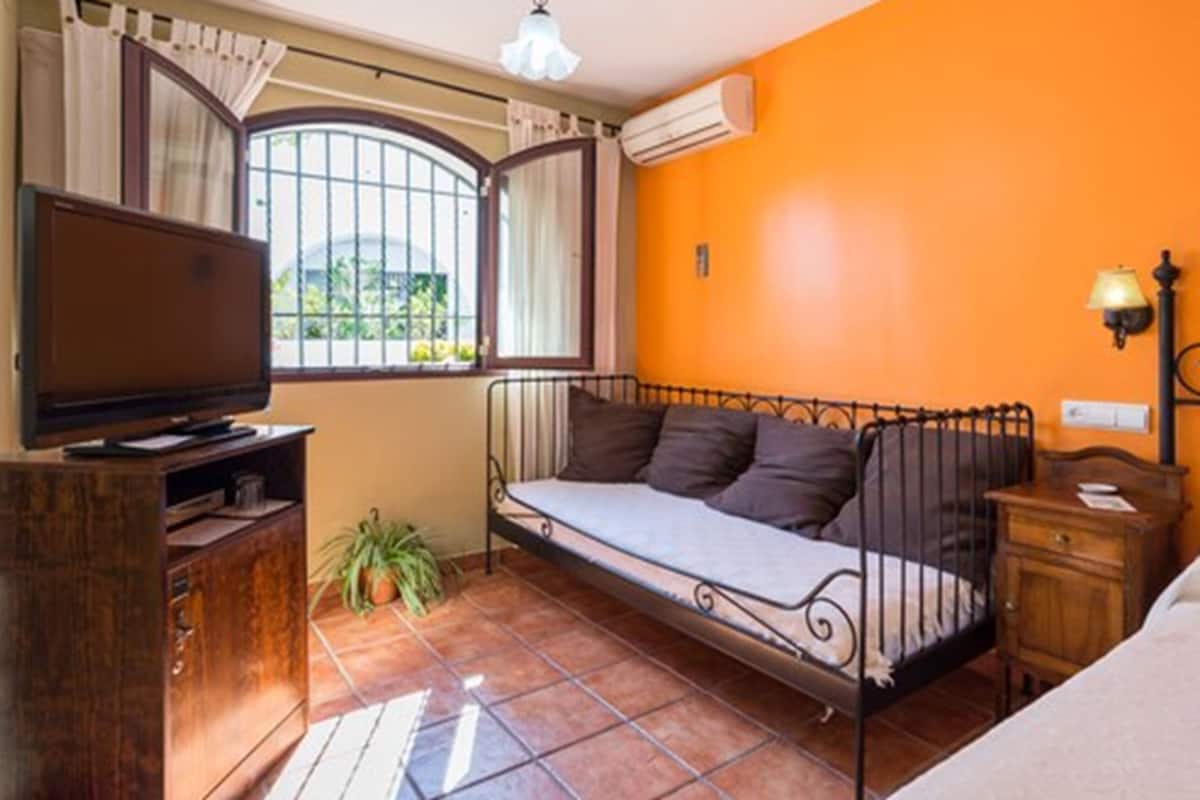 Una habitación con cama, televisión, una mesita y ventana con cortinas.