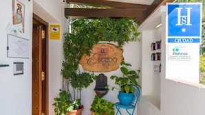 A small courtyard with a wooden sign reading "El Escudo de Mijas," potted plants, and a blue chair. - Hostel El Escudo de Mijas (Mijas)