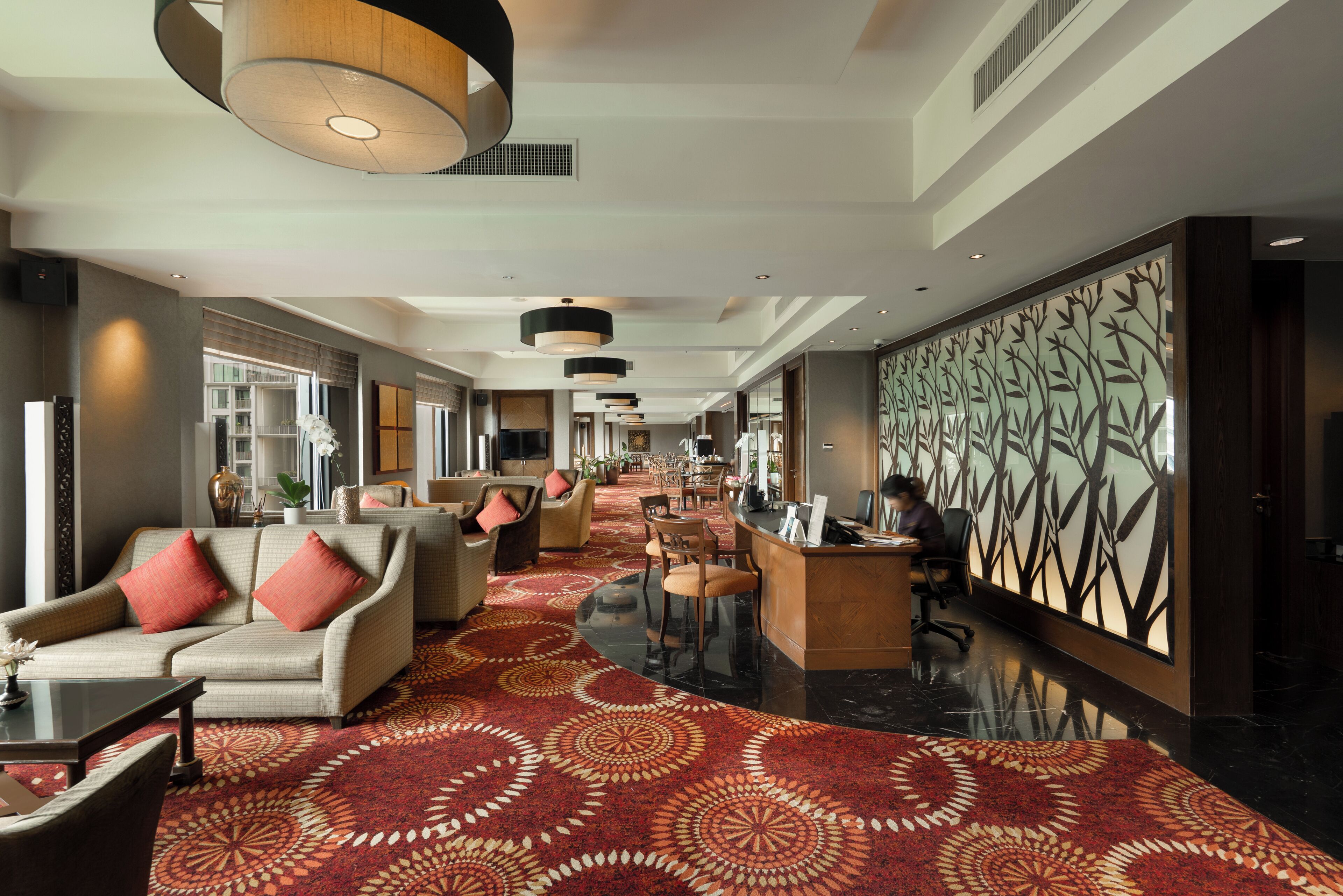 A hotel lobby with a patterned carpet, seating area with sofas and chairs, a reception desk, and a large decorative wall.