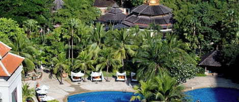 A resort with a large swimming pool surrounded by palm trees and covered seating areas.