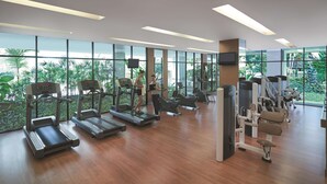Une salle de sport moderne équipée de tapis de course, d’appareils de musculation et de grandes fenêtres donnant sur un paysage verdoyant.