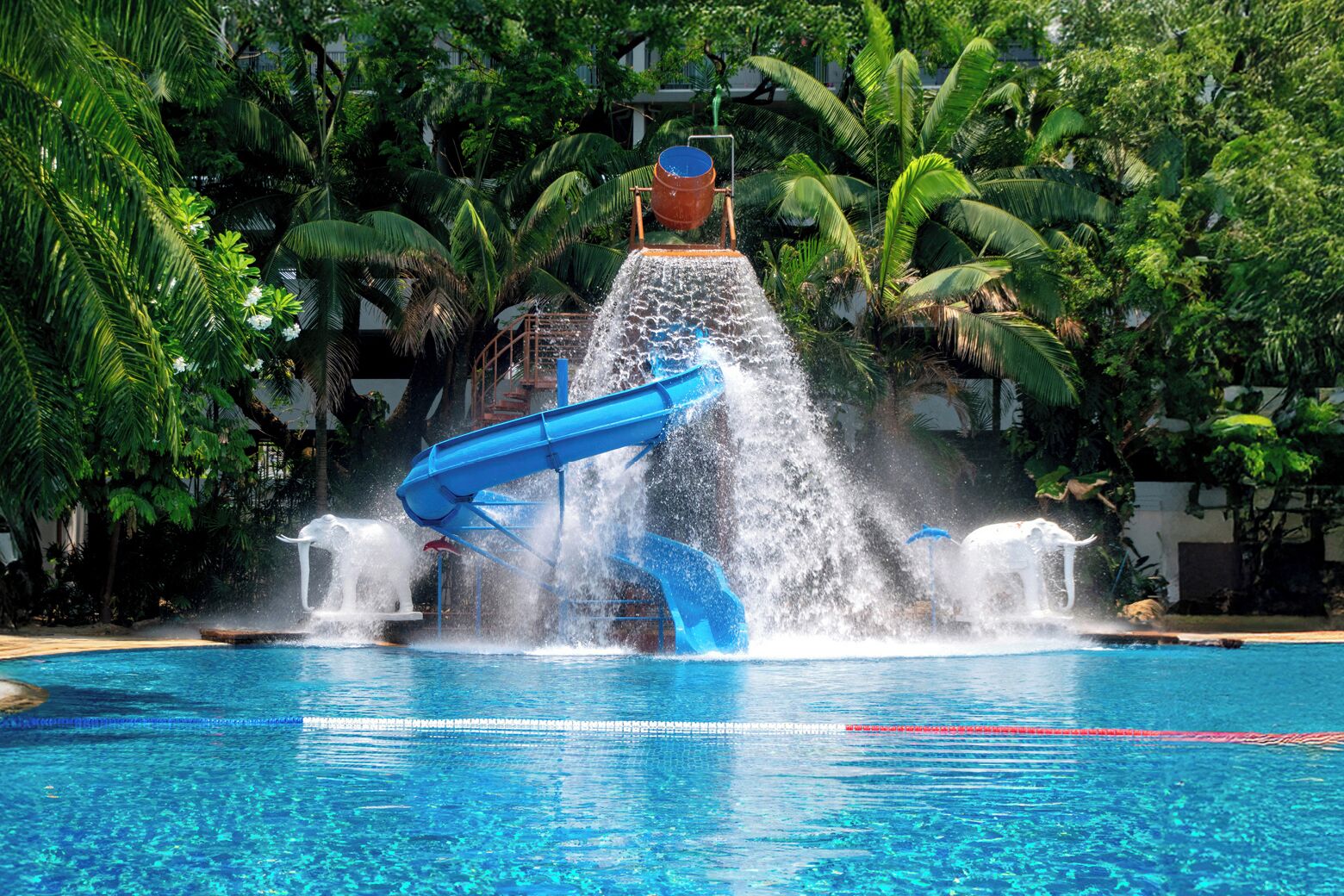 A water slide structure over a pool with surrounding lush greenery.