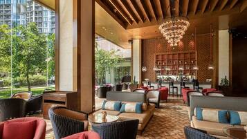A modern lounge area with wicker furniture, a bar, and a view of greenery.